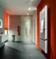 Vertikaler Kermi-Heizkörper in Weiß mit Längsrippen an der Wand, daneben ein Duschebereich und ein Waschbecken im modernen Badezimmerdesign.